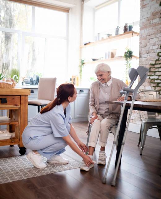 Pensioner smiling. Thankful beautiful pensioner smiling while caregiver lacing shoes for her